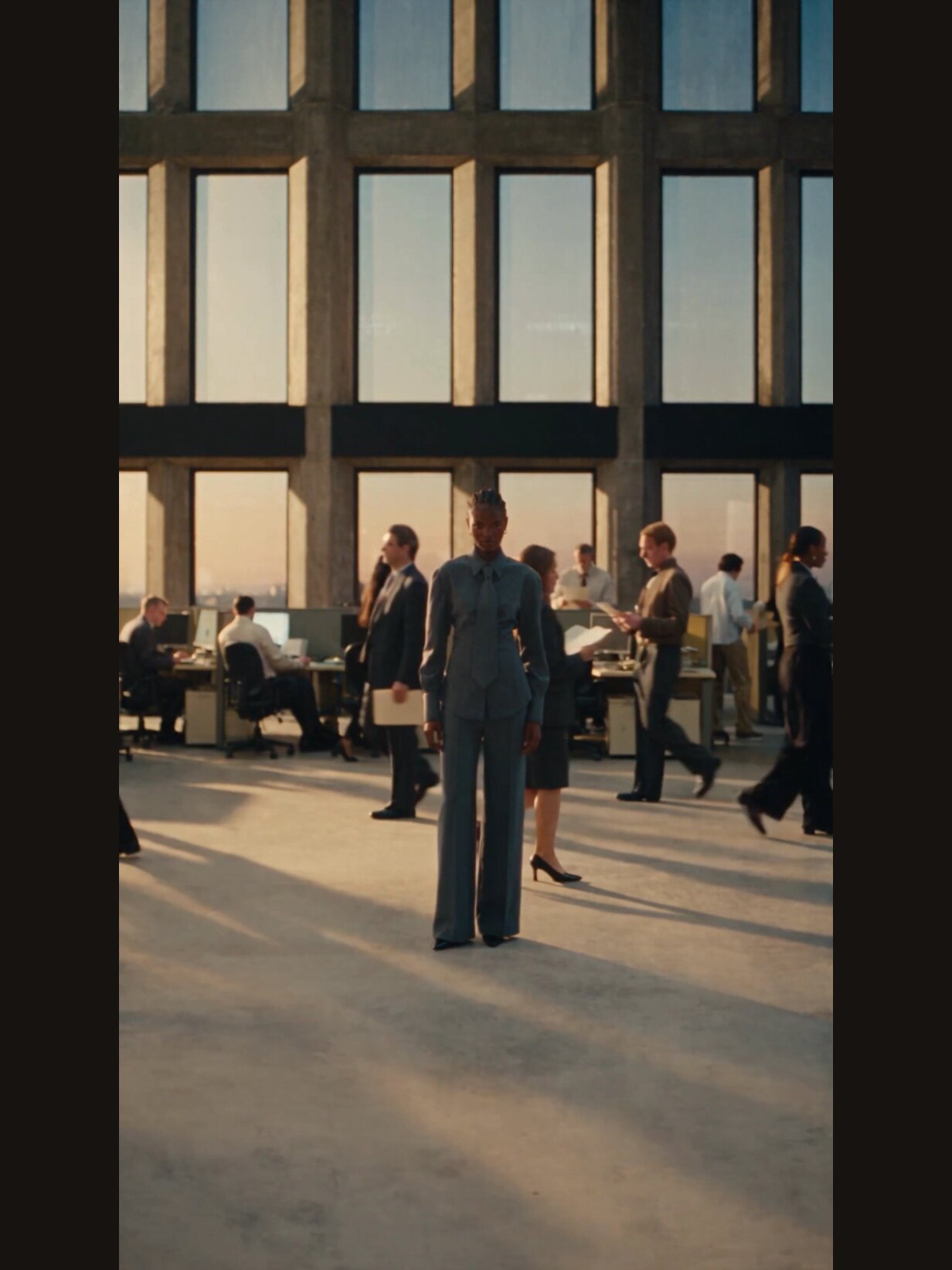 Opening frame of the campaign film: a model walking through an office floor at sunset.