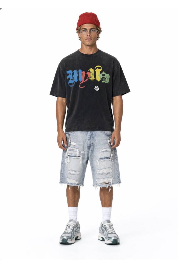 The same denim shorts on a model against a plain white studio background, worn with a black graphic t-shirt, white socks and grey trainers.
