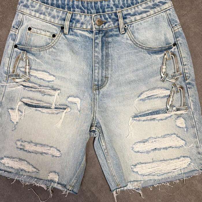 Close crop of the shorts as photographed on the floor: two carabiners, and horizontal slash rips across both legs.